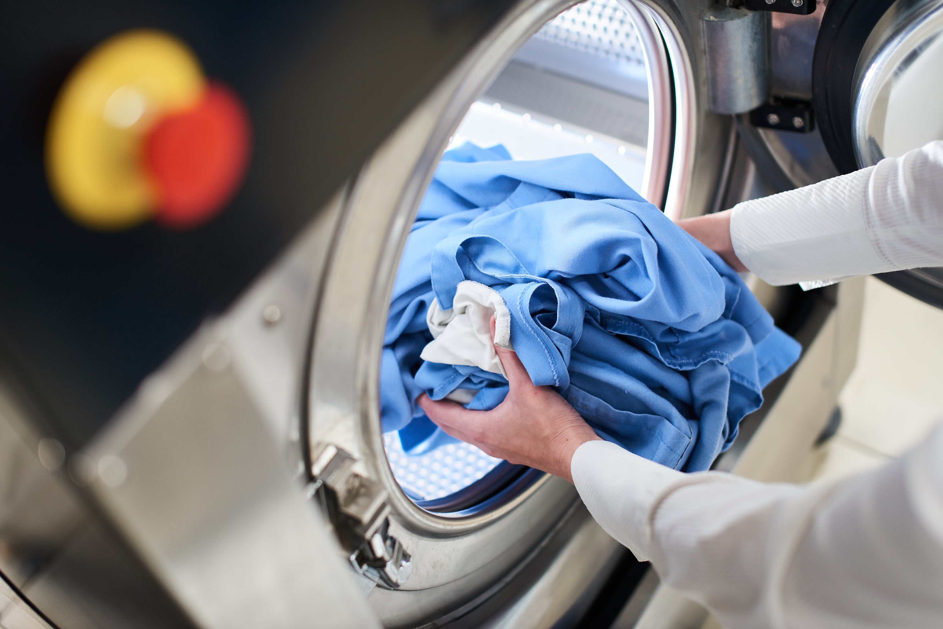 Clean and Clear Laundry Person loading blue clothes into a washing machine