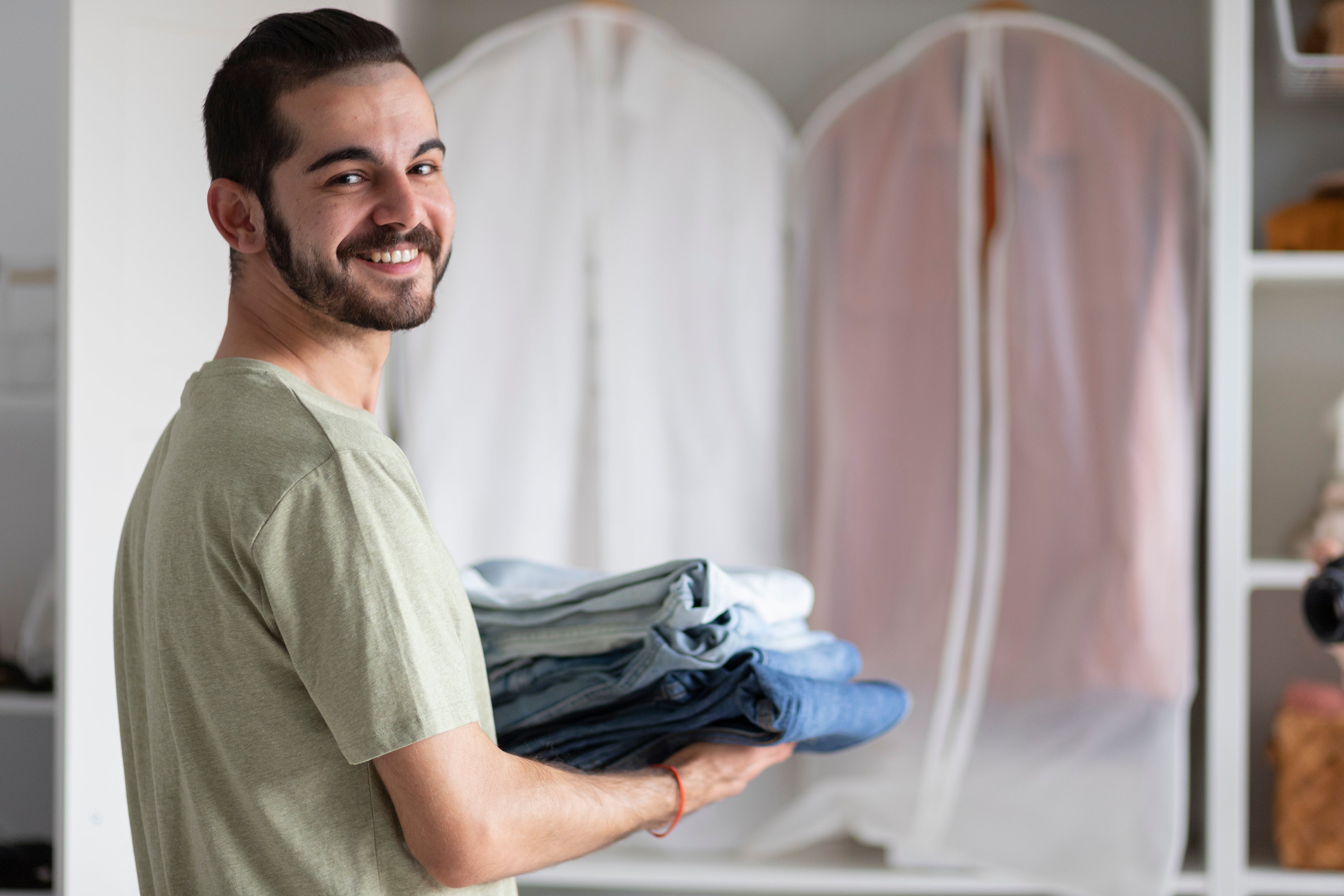 Happy Man holding folded clothes in a room with hanging clothes in the background